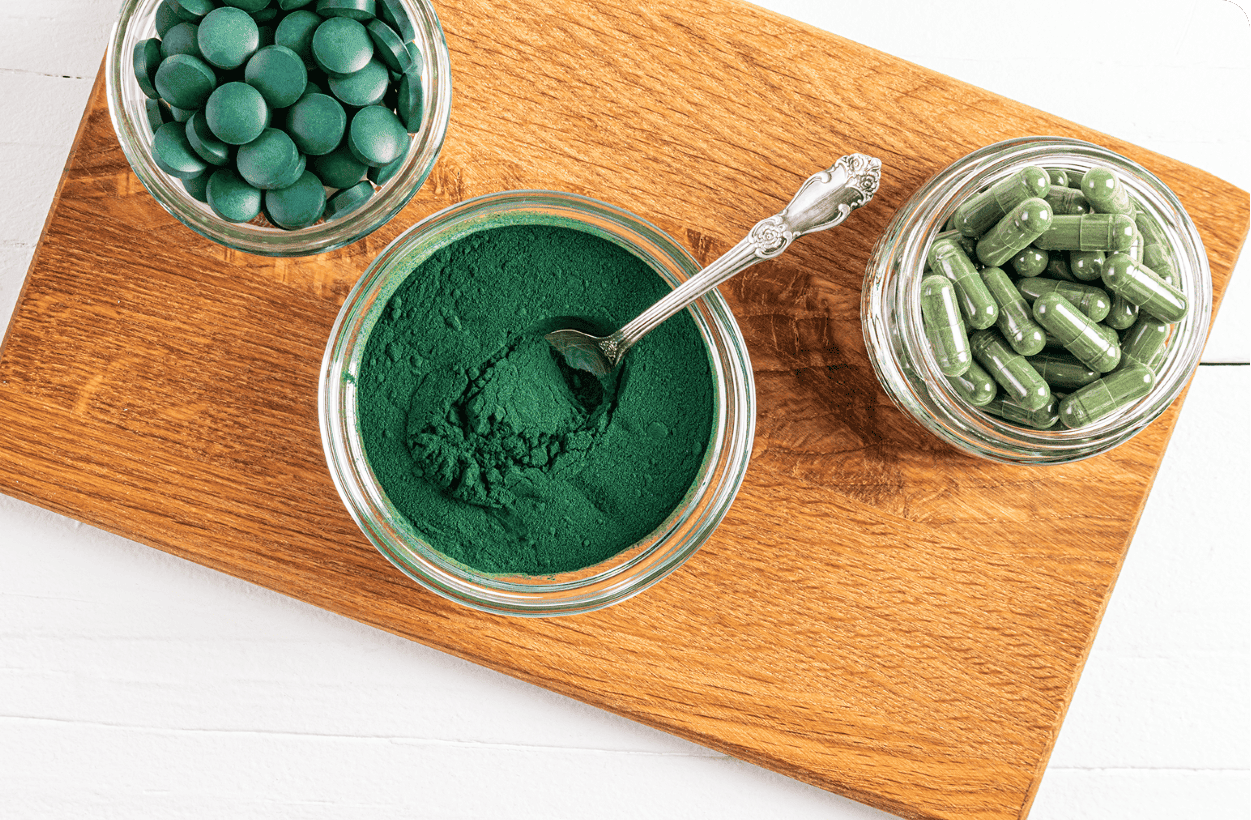 support en bois avec trois contenants. spiruline en comprimés. spiruline en poudre. spiruline en gélules.